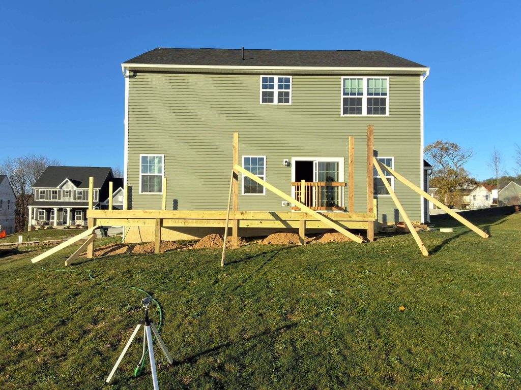 Elevated deck framing on sloped yard with pressure-treated posts and beams during construction