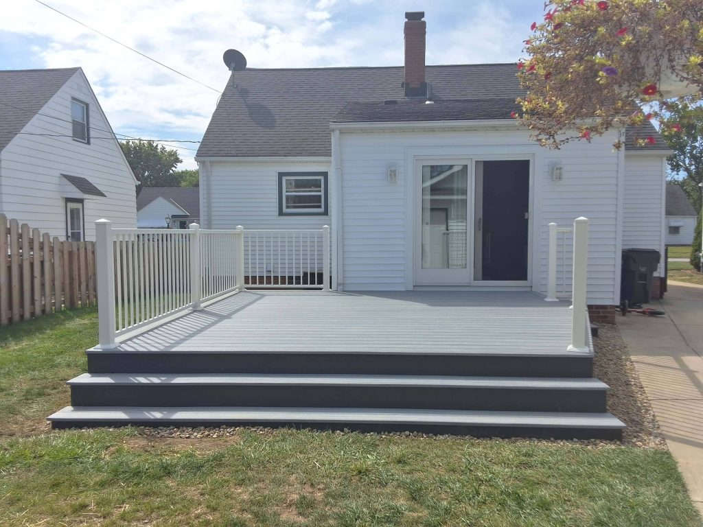 Gray composite backyard deck with white vinyl railings and wide three-step entry at a ranch home