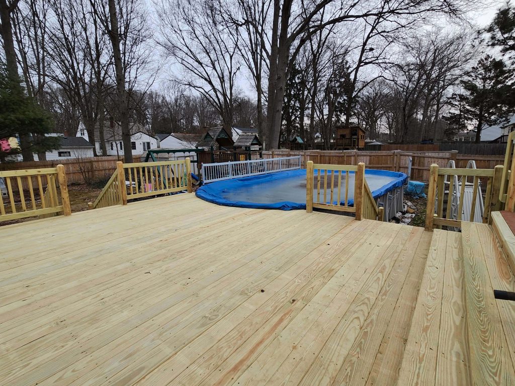 Large pressure-treated pool deck with safety railings surrounding above-ground swimming pool
