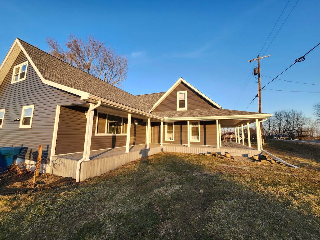 Updated dark-gray vinyl siding with white trim on farmhouse featuring a wraparound porch